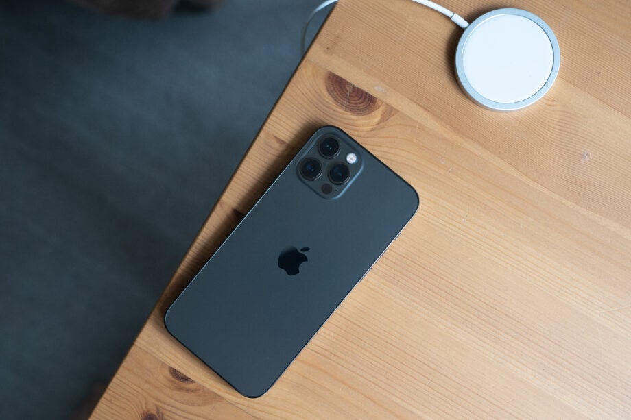 A black and gray iPhone 12 Pro laid upside down on a wooden table, view from top