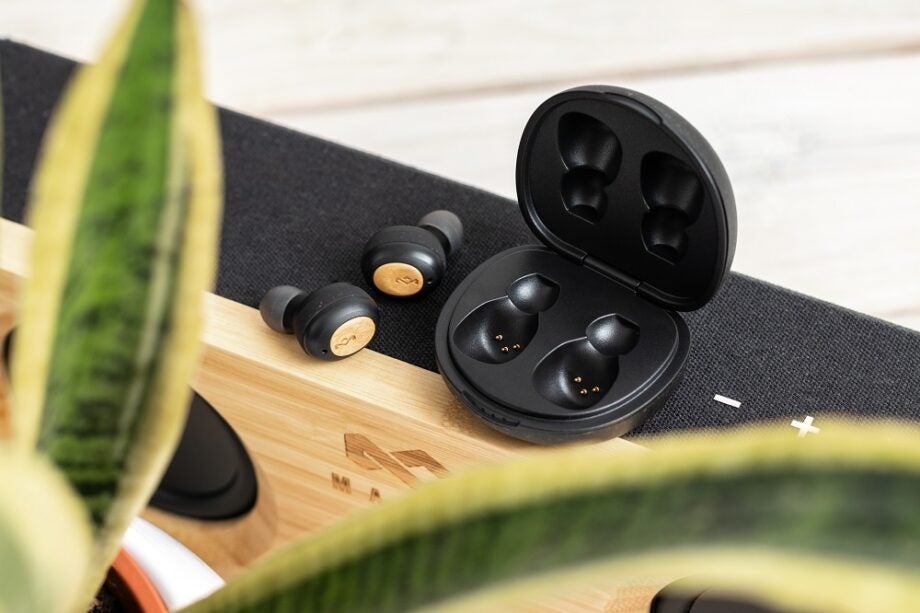 Black-brown House of Marley Champion earbuds resting beside it's case on a table