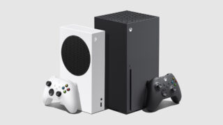 A black Xbox with it's controller beside standing against a white Xbox with it's controller beside