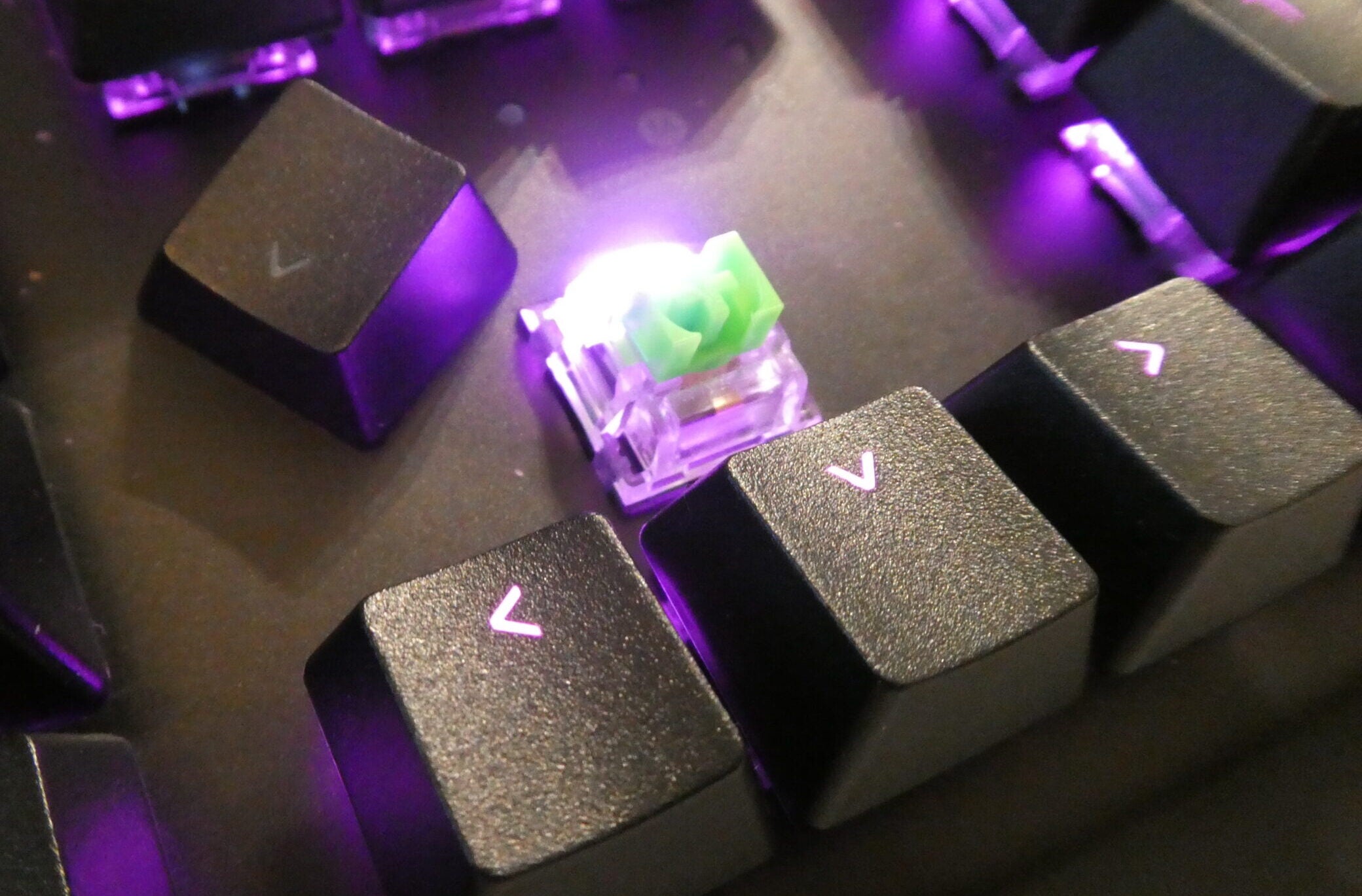 Close up image of a removed key from a black BlackWidow V3 Pro keyboard with purple lights beneath the keys