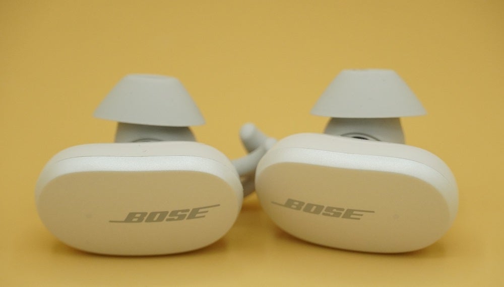 White Bose QuietComfort earbuds resting on yellow background
