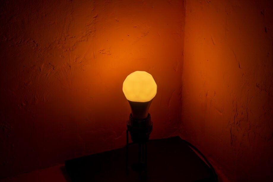 A Nanoleaf colored bulb fixed in a holder kept in a corner, lit up with red color