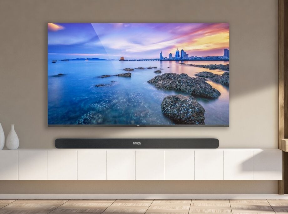 A black TCL-TS8111 TV hanging to a wall with a black soundbar placed below