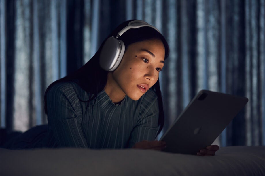 A girl laid on bed, holding in iPad, wearing Apple AirPods Max