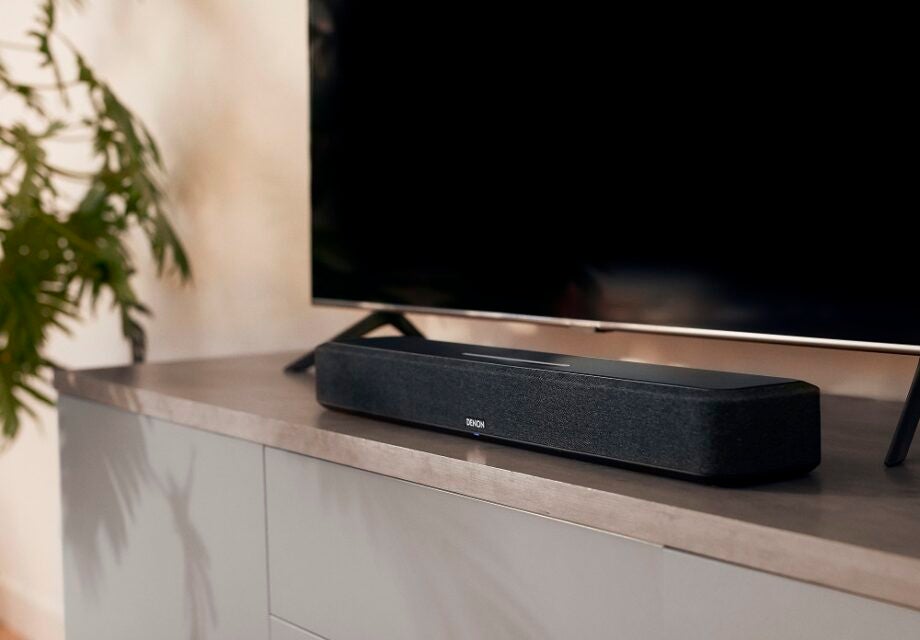 A black Denon Home 550 soundbar kept on a wooden table in front of a black TV