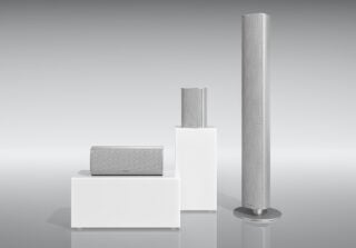 Three different shaped and sized silver PIEGA Ace speakers standing on white background