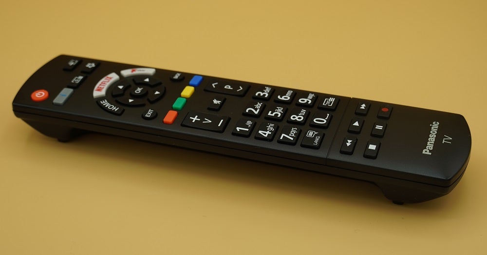 A black Panasonic HX600 TV's black remote resting on yellow background