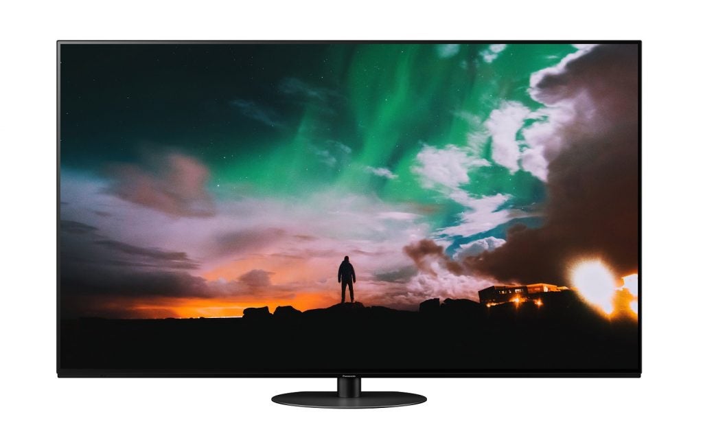 A black Panasonic JZ980 TV standing on a white background displaying a man standing on stones at dawn