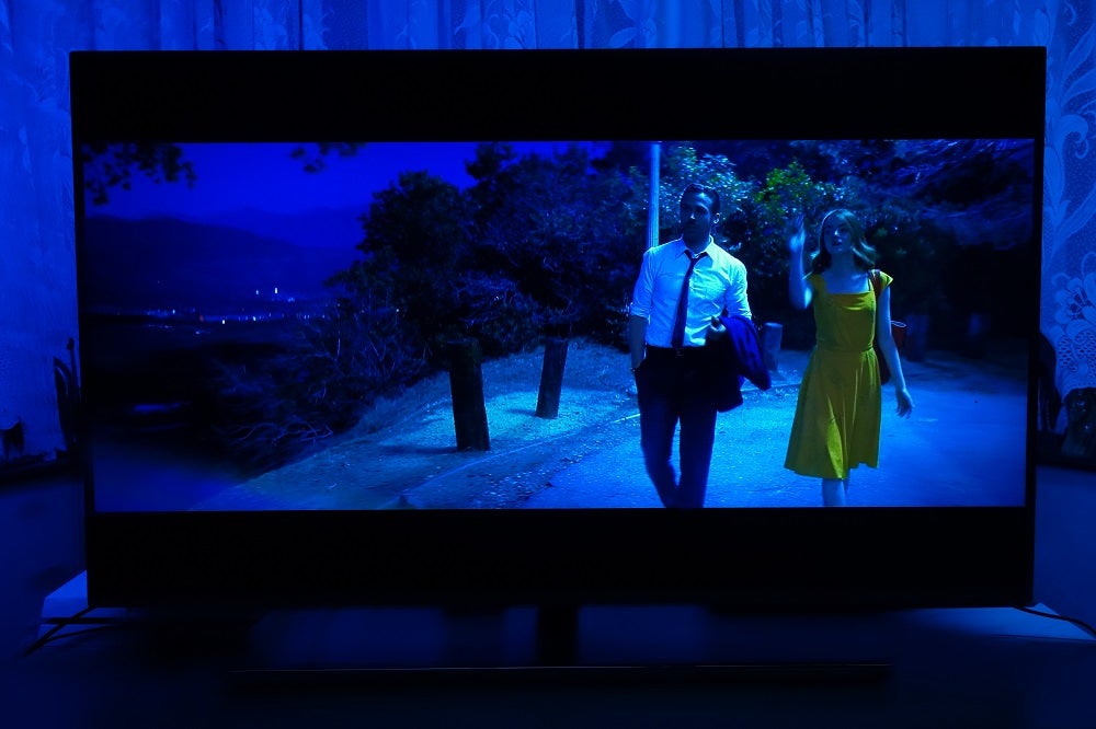 A black Philips 50PUS8545 TV standing on table, displaying a guy and a girl walking at night