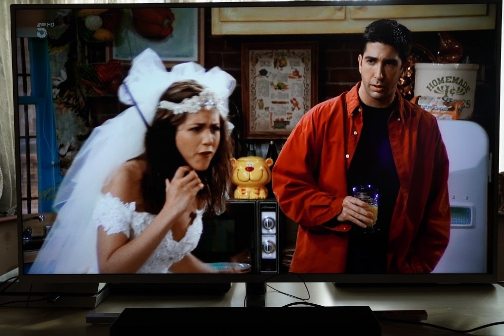 A black Philips 50PUS8545 TV standing on table, displaying a scene from friends