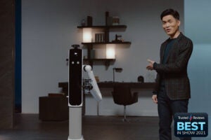A black and white Samsung bot named handy standing in a rook with a man standing beside