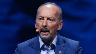 Close up image of Peter Moore in blue outfit, speaking with a mic attached to his right ear