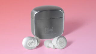 Close up image of Klipsch T5 earbuds resting on pink background with it's case resting behind