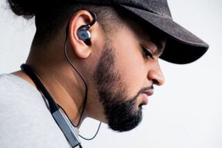 A bearded man in cap, wearing Ausounds AU-flex ANC earphones, right side view