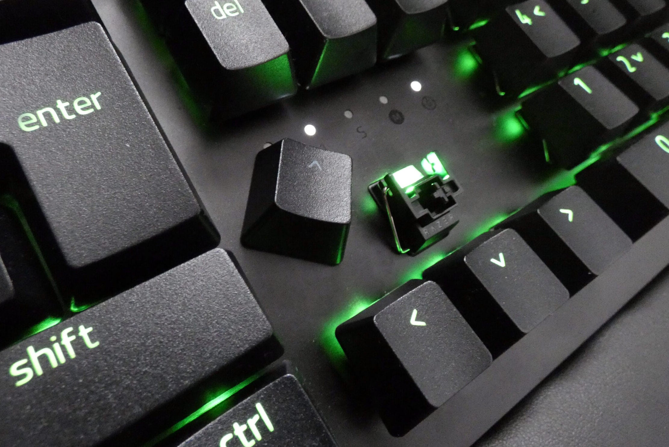 Razer Huntsman V2 AnalogClose up image of a removed key from a black Huntsman V2 analog keyboard with green lights beneath the keys