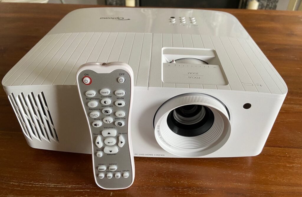 The Optoma UHD38 projector and remotefront and top  view of cool white projector with the lense in clear sight plus it's remote control leaning slanted to it
