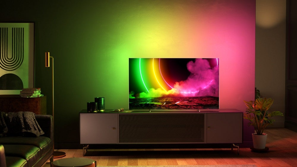 A silver Philips OLED806 TV standing in a colorful background, displaying a colorful wallpaperA Philips OLED806 standing on a table, displaying a colored wallpaper with its light escaping from TV to room