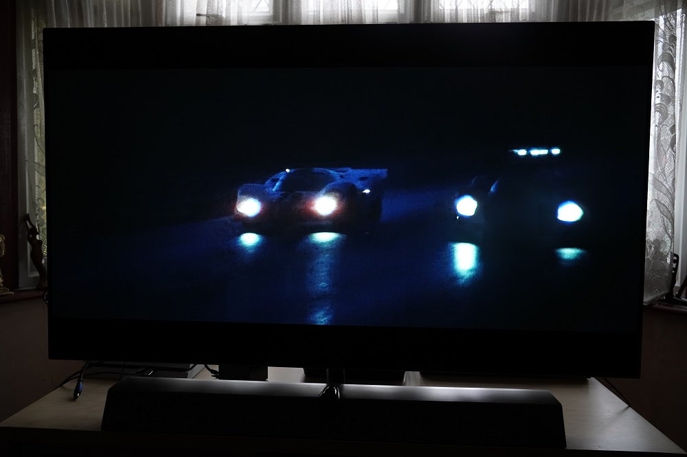 A black Philips OLED935 standing on a table, displaying a scene from Le Mans