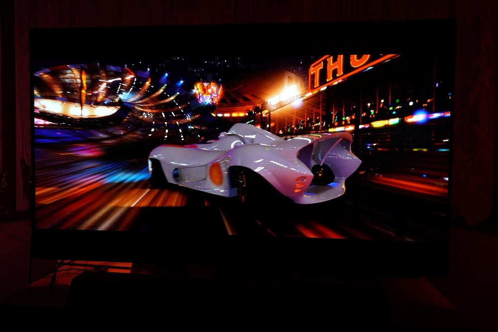 A black Philips OLED935 standing on a table, displaying a scene from Speed Racer
