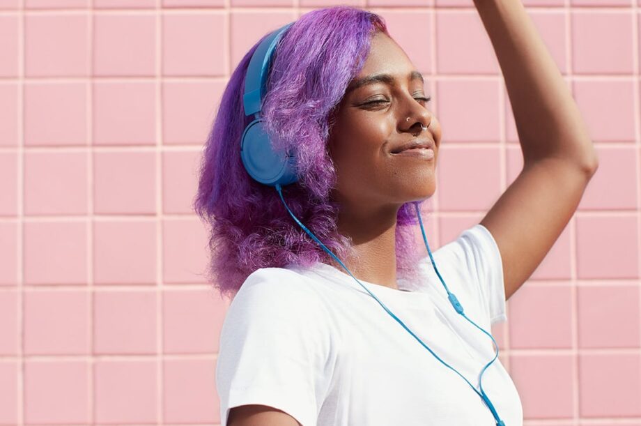 chocolate skinned purple hair girl enjoying the smooth sounds of music through comfortable blue head sets
