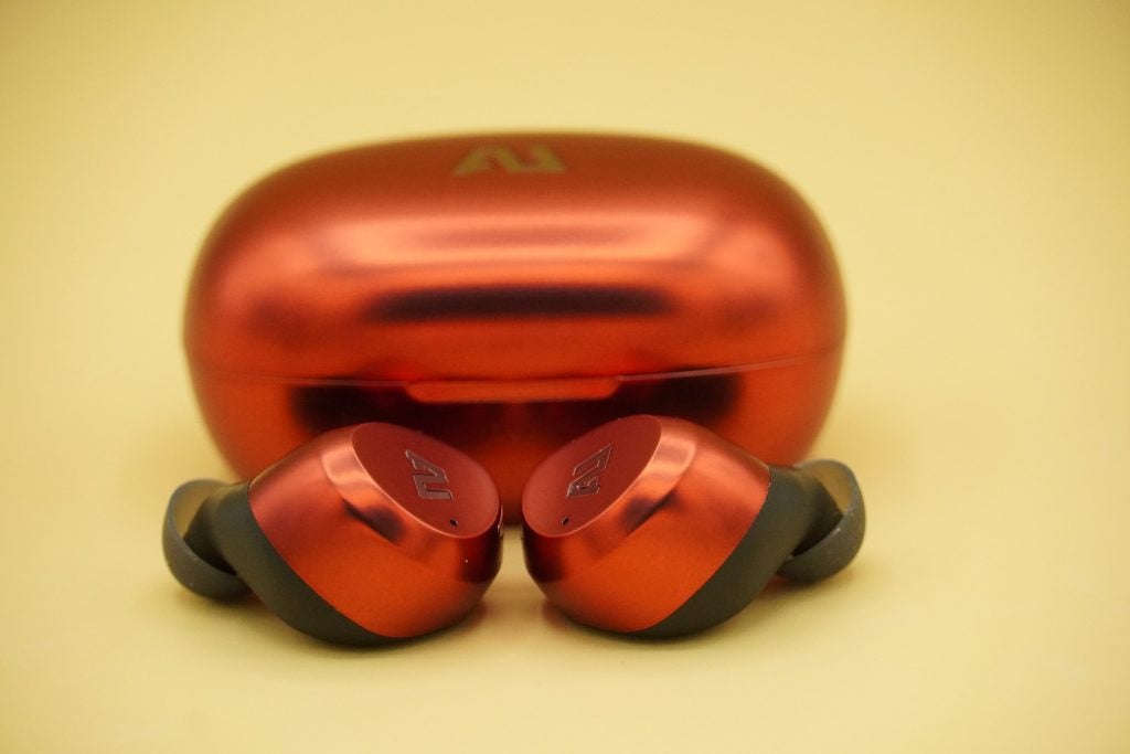 Ausounds AU stream hybrid orange-brown earbuds resting on a table, with it's case standing behind