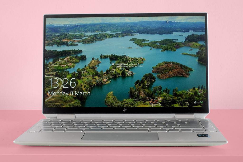 A silver HP spectre X360 laptop on pink background, displaying date and time on lock screen