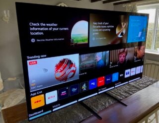 A black LG OLED 65G1 TV standing on a table, displaying trending now content and app list