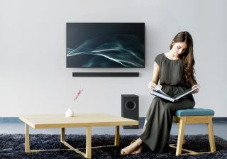 A black Panasonic HTB490 TV mounted to a wall with a lady sitting on the fron reading a book