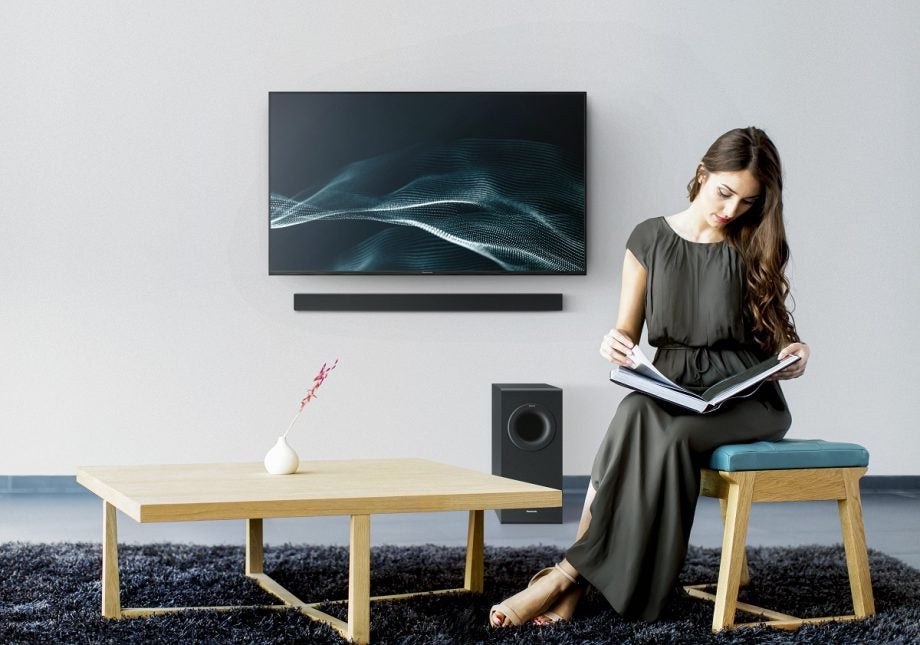 A black Panasonic HTB490 TV mounted to a wall with a lady sitting on the fron reading a book