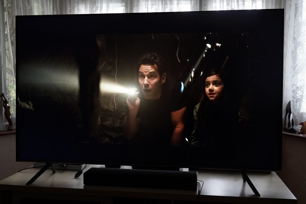 A black Samsung Q65T TV standing on a table, displaying a scene from Ant Man
