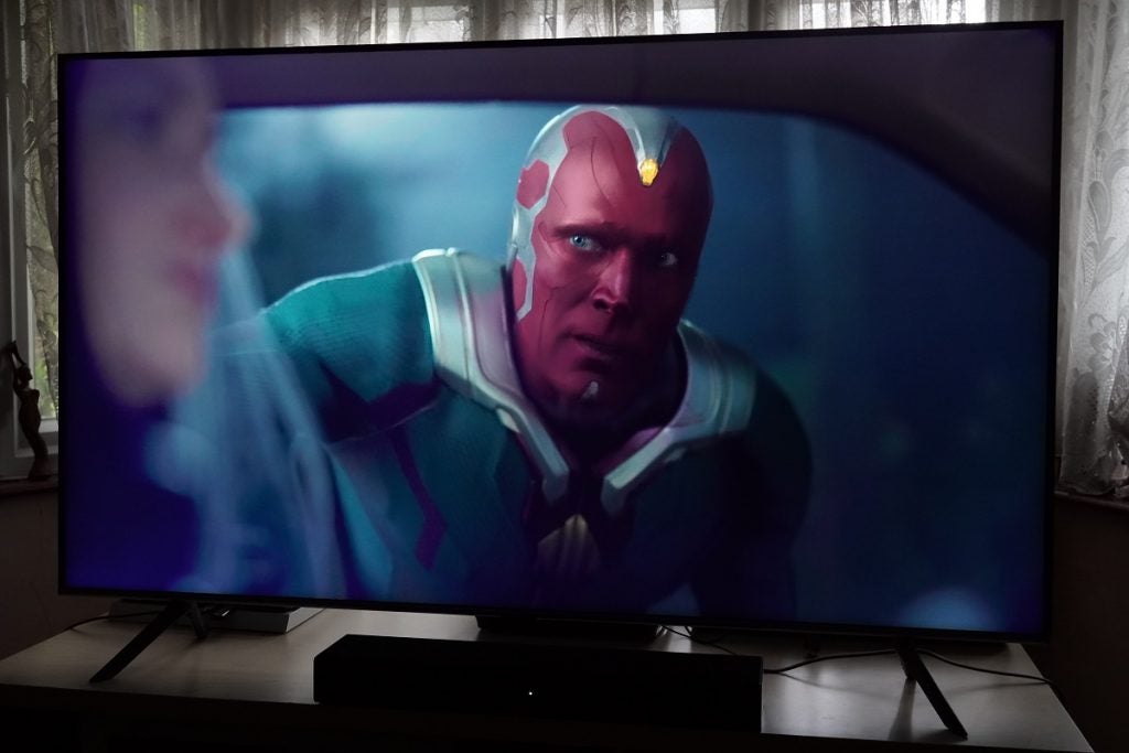 A black Samsung Q65T TV standing on a table, displaying a scene of Marvel Vision