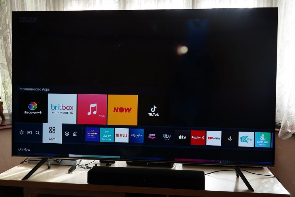 A black Samsung Q65T TV standing on a table, displaying recommended apps and installed aps