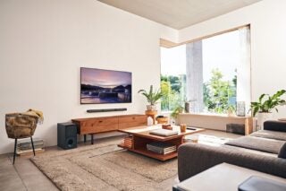 Black Sony HT S40R speakers standing in a room beside a table and mounted to wall below TV