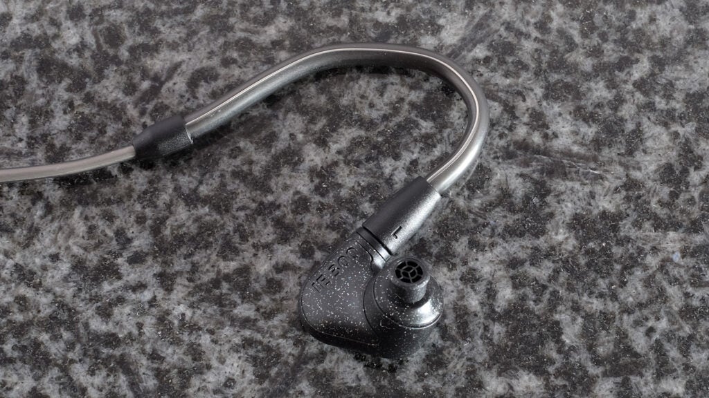 Gray and black earphone resting on black backround, front side view