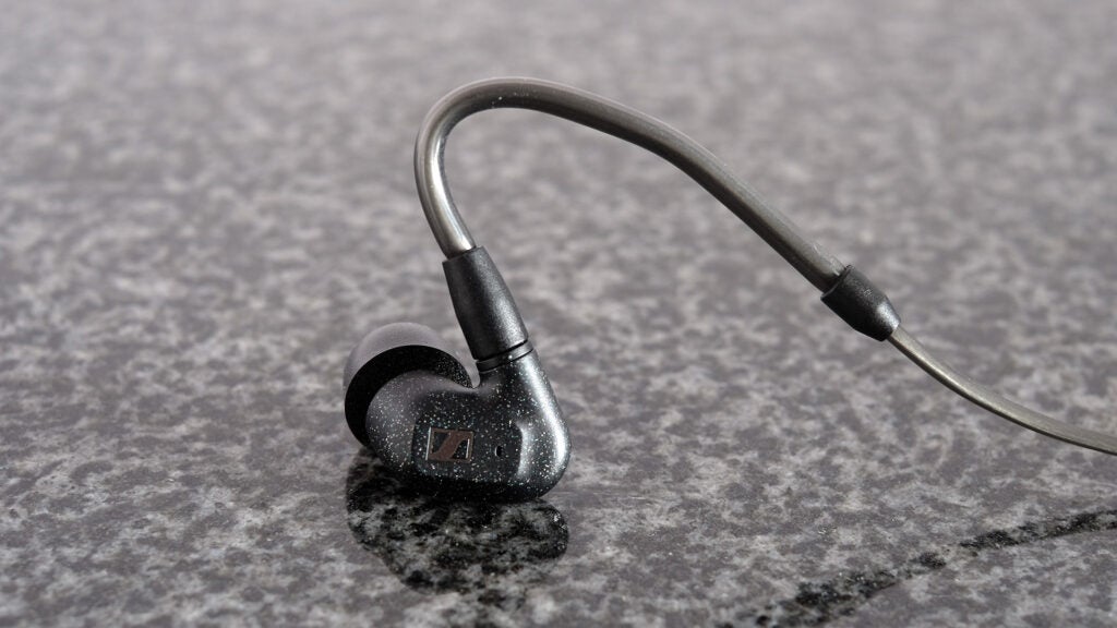 Gray and black earphone resting on black backround, back side vertically standing view