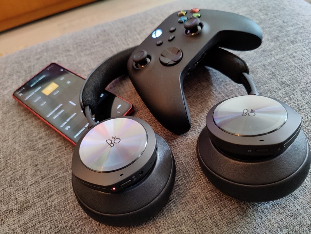 BO Beoplay black headphones, black XBOX controller on the top, and a smartphone at the back 