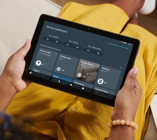 A women in yellow outfit sitting on a couch holding a Amazon Fire HD10 tablet displaying device dashboard
