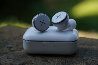 Kygo Xellence wireless white earbuds resting on top of it's white case resting on ground