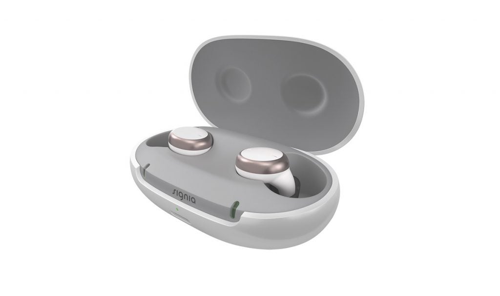 Silver and white Signia active Pro hearing aids earbuds resting in silver and white case with lid open on a white background