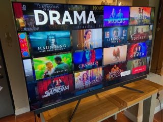TCL65C815 TV standing on a wooden table, displaying drama series