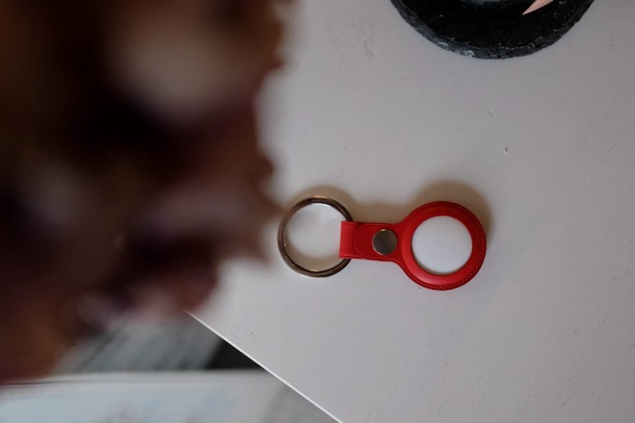A white Airtag placed upside down in a red holder, attached to a key chain, placed on a white table, view from far top