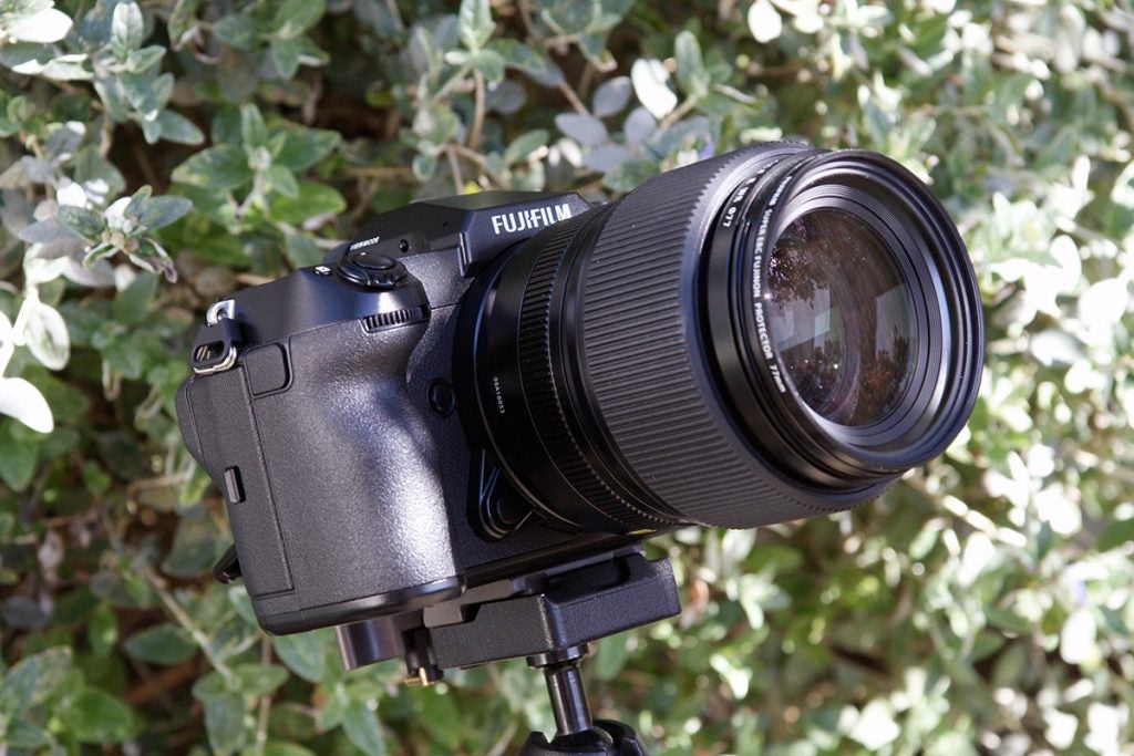 Front left side view of a black Sony GFX 100 standing on a stand