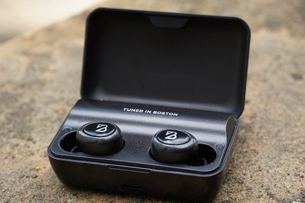 Front right view of black Bay duet 50 pro earbuds resting in its case with lid open resting on ground