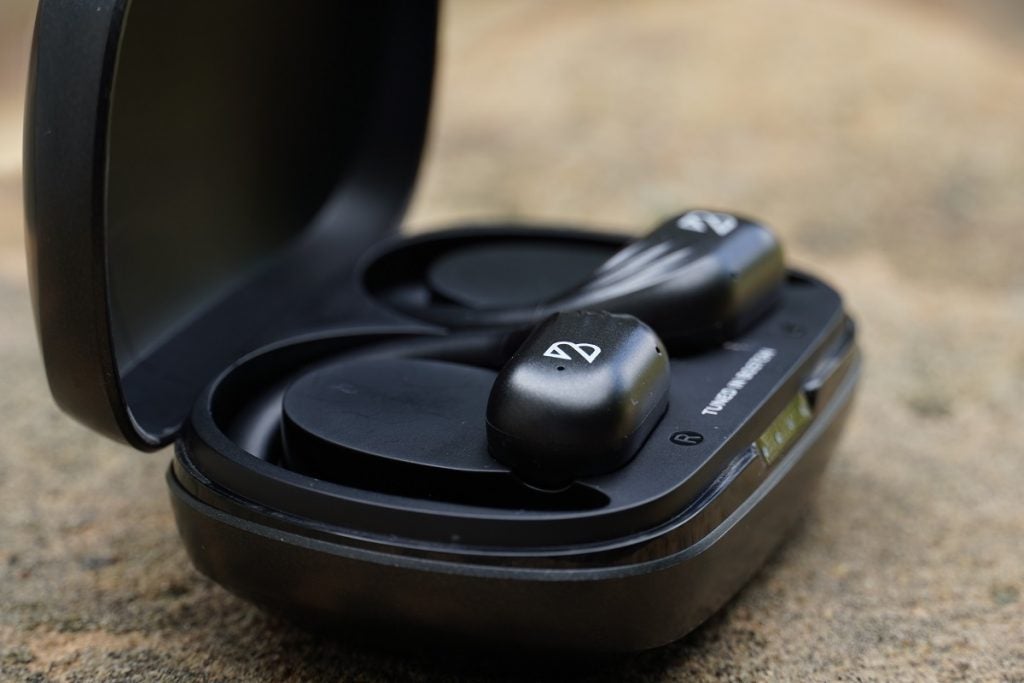 Black Bay's runner 60 wireless earbud's black case resting on ground, left side view, lid open and earbuds resting in case can be seen