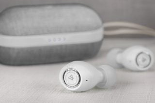 White Lypertek PurePlay Z3 2.0 earbuds placed on a white table with its grey and white case partially visible on the back