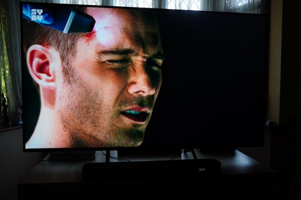 A black Panasonic TX 65HX940B TV standing on a wooden table displaying a scene from Killjoy