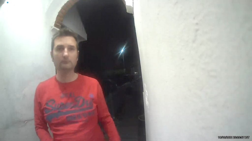 Ring Video Doorbell Night Sample with Floodlight Turned OnA man in a red t-shirt, standing on the front door at night, looking towards the camera of Ring video  doorbell, showcasing night sample with floodlight turned on
