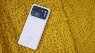 Back side view of a white Mi 11 Ultra pro with  two camera and flashight on the back and a mini screen on the side displaying date and time with battery