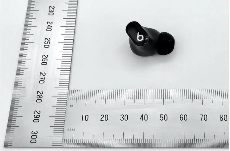 A black earbud from Beats studio buds 1 resting with two scales aligned at the left and bottom