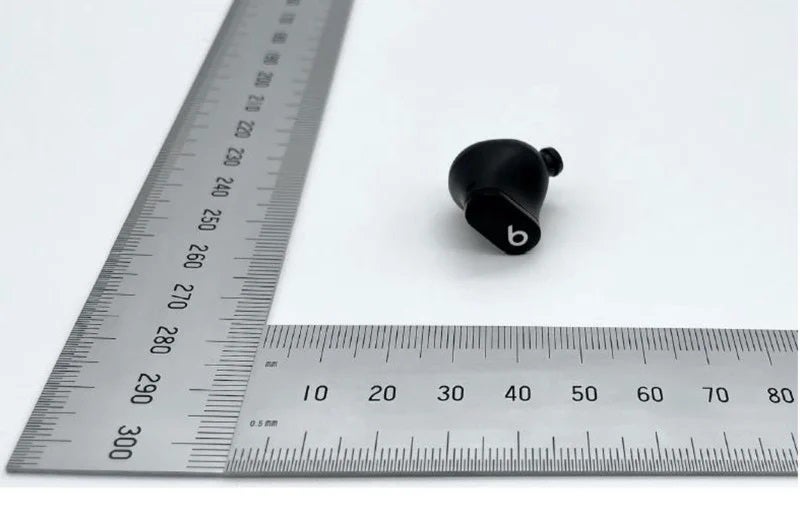 A black earbud from Beats studio buds 2 resting with two scales aligned at the left and bottom
